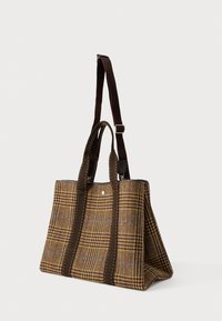 Καφέ καρό τσάντα ώμου με σκούρους καφέ ραφές στις λαβές και ρυθμιζόμενο λουρί στον ώμο, τοποθετημένη όρθια σε λευκό φόντο.