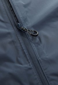 Tmavomodrá bunda na zips s hladkým vodeodolným materiálom. Má výrazný zips s háčikovým ťaháčikom a textúrovaný bočný panel.