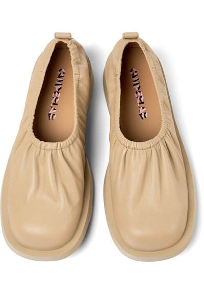 Beige läderslip-on skor med draperad ovandel, rund tå och vadderad sula. Inuti finns en logotyp i kontrasterande färg.