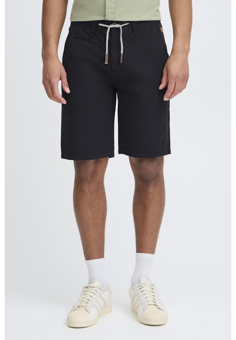 Svarte shorts laget av lett stoff, med snøring i livet, sidelommer og rett snitt, brukt med hvite sneakers og sokker.