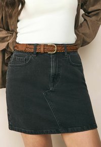 Svart denim minikjol med en åtsittande design, två framfickor och ett flätat brunt läderbälte med ett guldfärgat spänne.