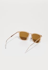 Ochelari de soare cu nuanțe de maron, cu rame metalice clare și aur rose, design unghiular, accente decorative pe față și brațe subțiri din fir.