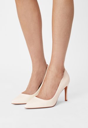 Puntige hakken in zacht wit leer. Heeft een slank ontwerp en een slanke stilettohak. Gladde textuur met minimale details.