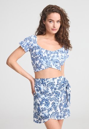 Top corto a maniche corte puffate con motivo paisley blu e bianco, abbinato a una gonna avvolgente coordinata con dettaglio di legatura.