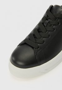 Baskets en cuir noir avec bout rond, tige texturée, lacets noirs plats et semelle en caoutchouc blanche. Présente un texte en relief sur le talon.
