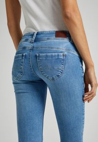 Modré džíny z denimu s přiléhavým střihem, s zadními kapsami s křivkovým švem a hnědou koženou nášivkou značky na pase.