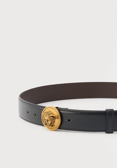 Μαύρη δερμάτινη ζώνη με στρογγυλή χρυσή αγκράφα που διαθέτει ανάγλυφο κλασικό σχέδιο κεφαλιού Μέδουσας.