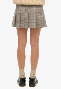 Ruitenrok mini met plooien, in beige, bruin en blauw. Gemaakt met zwarte schoenen en geribbelde beige sokken.