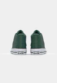 Ténis de cano alto em tela verde com solas de borracha branca. Apresenta uma textura suave, bico redondo e detalhes em preto com a marca "CONVERSE ALL STAR".