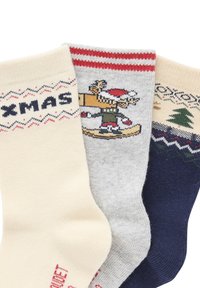 Three pairs of cotton socks: cream with "XMAS" text, gray with a festive reindeer design, and navy with a tree motif. Textured patterns combined.