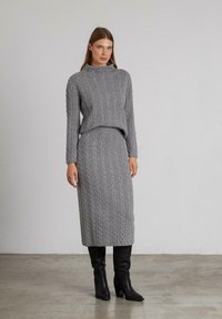 Grijs gebreid trui- en rok set met een kabelbreipatroon, hoge hals, lange mouwen en knielange zwarte laarzen. Gladde textuur.