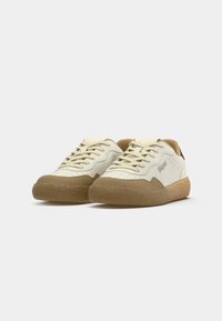 White sneakers with tan suede accents, featuring a smooth leather upper, flat laces, perforated toe box, and a textured rubber sole.