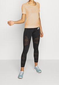 Meruňkový síťovaný top s krátkým rukávem a logem "NIKE". Černé legíny s vzorem "NIKE AIR". Světle modré tenisky. Sportovní design, přiléhavý střih.