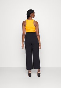 Un débardeur orange ajusté associé à un pantalon noir ample à jambes larges, mettant en avant une texture lisse et un design minimaliste.