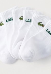 Άσπρες βαμβακερές κάλτσες με πράσινο κεντημένο λογότυπο Lacoste και κροκόδειλο, με ριμπ μανσέτες και μαλακή υφή. Σετ πέντε ζευγαριών.
