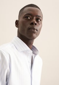 Camicia a righe azzurro chiaro con base bianca, colletto con bottoni, tessuto textured e forma aderente, con patta frontale.
