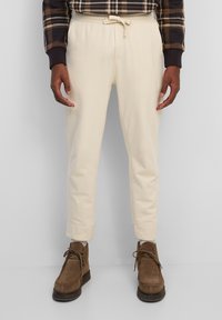 Cremfarbene Sweatpants mit einem Kordelzugbund, schmal zulaufenden Beinen und gerippten Bündchen, kombiniert mit braunen Wildlederstiefeln. Strukturiert stoff.