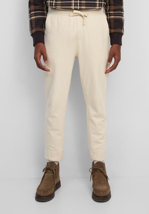 Cremfarbene Sweatpants mit einem Kordelzugbund, schmal zulaufenden Beinen und gerippten Bündchen, kombiniert mit braunen Wildlederstiefeln. Strukturiert stoff.