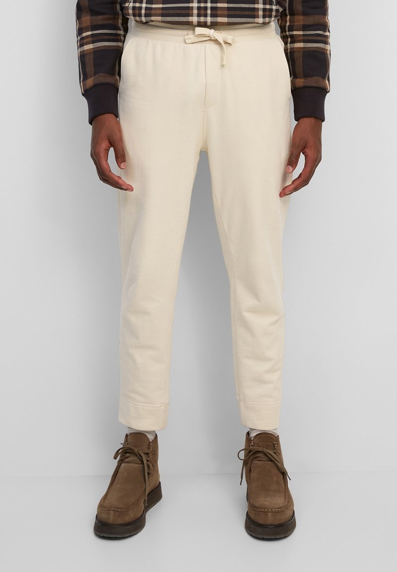 Cremfarbene Sweatpants mit einem Kordelzugbund, schmal zulaufenden Beinen und gerippten Bündchen, kombiniert mit braunen Wildlederstiefeln. Strukturiert stoff.