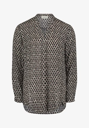 Blusa de mujer de manga larga con patrón de rombos en negro y blanco y sutiles detalles en rosa, con cuello de solapa y corte holgado.