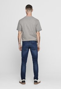 Camiseta gris de manga corta combinada con jeans oscuros. El conjunto presenta un diseño simple, con una textura suave y un ajuste estándar.