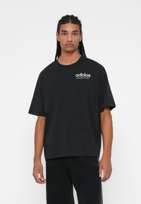 Črna oversize majica s kratkimi rokavi iz bombaža, z okroglim izrezom. 'adidas' logo v beli barvi natisnjen na zgornji levi strani.