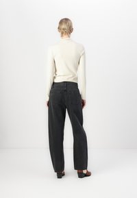 Black high-waisted jeans with a relaxed fit, featuring a straight leg design and two back pockets, paired with a cream ribbed long-sleeve top.