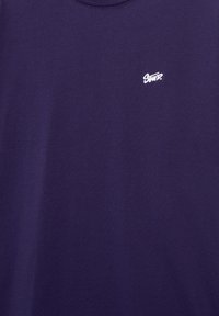 Dark purple fabric with small white embroidered logo reading "Stmp." on upper left side.