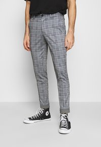 Grå rutiga byxor med rak passform, tillverkade av lätt materiale. Har uppvikta fållar och en knappstängning, kombinerat med svarta sneakers.