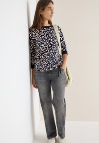 Suéter azul marino con un diseño de leopardo beige, combinado con jeans rectos de color gris claro. El conjunto se complementa con un bolso claro.