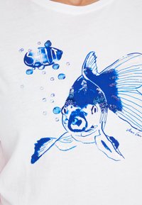 White t-shirt featuring a blue fish graphic with sequins, surrounded by bubbles, and the word “Salut” in stylized blue text above.