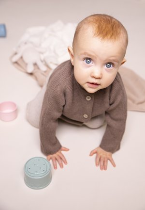 Brauner gestrickter Cardigan mit Knöpfen, graue Hose und blaue Augen. Leichter mintfarbener Spielzeugbehälter in der Nähe auf einem neutralen Hintergrund.