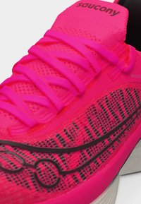 Φωτεινό ροζ αθλητικό παπούτσι Saucony με υφασμάτινη υφή, κορδόνια σε αντίστοιχο ροζ χρώμα και μαύρες λεπτομέρειες λογότυπου στη πλευρά.