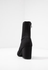 Černá kotníková bota vyrobená z elastického materiálu, s blokovým podpatkem a bočním zipem. Hladký povrch s elegantním, zúženým designem.