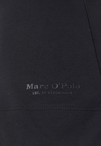 Czarna odzież sportowa z gładką teksturą, z wytłoczonym logo "Marc O'Polo" oraz napisem "EST. W STOCKHOLM" w eleganckim designie.