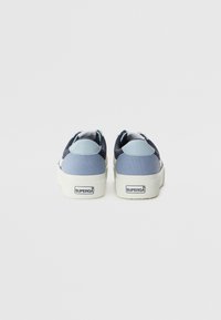 Blå kanvas sneakers med kontrasterende lyseblå detaljer, en hvit gummisåle og en logo på hælen. Lågt toppdesign, ingen synlige snørebånd.