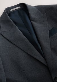 Blazer gris foncé texturé avec col à revers cranté, doublure noire et pochette assortie glissée dans la poche poitrine.