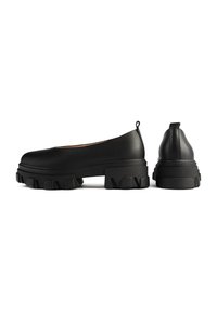 Zapatos de plataforma negros con un suave upper de piel sintética, puntera redondeada y suela texturizada tipo lugs. Incluye una pequeña lengüeta en el talón para facilitar el calzado.