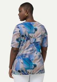 Camisa de manga corta en tejido ligero con un patrón floral en tonos de azul, beige y crema, con un corte relajado y escote redondo.