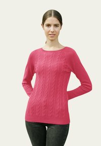 Pull en tricot cablé fuchsia à manches longues, col rond et ourlet côtelé, associé à un jean foncé. Texture lisse, motif de point uniforme.