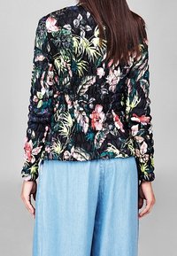 Blomstrete quiltet jakke i sort med livlige pink og grønne mønstre; har ribbet krave, elastiske manchetter og en figursyet silhuet.