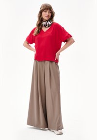 Czerwona krótkozasięgowa bluzka z dekoltem w serek połączona z beżowymi spodniami typu wide-leg. Stylizację dopełnia wzorzysty szalik na szyi.