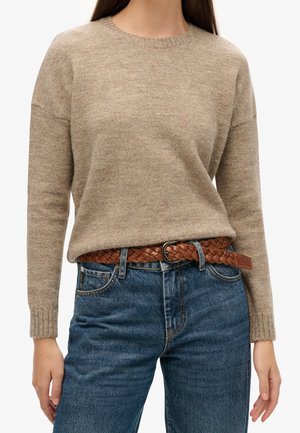Suéter de punto beige con cuello redondo y puños acanalados, combinado con jeans azules y un cinturón de cuero trenzado marrón.