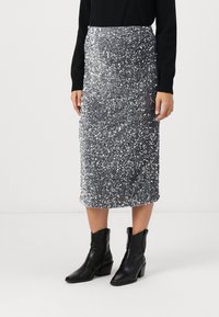 Gonna midi in paillettes argento con un design aderente e superficie testurizzata. Abbinata a stivali neri alla caviglia, creando una silhouette elegante.