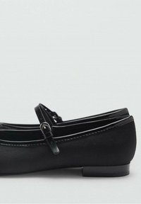 Zapatos planos negros Mary Jane con una delgada correa en el tobillo y hebilla plateada, acabado texturizado y tacón bajo sobre un fondo claro.