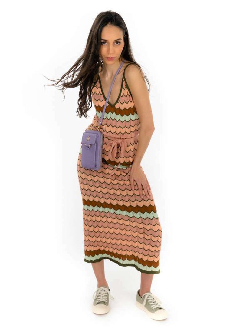 Femme portant une robe midi sans manches à motifs, des baskets beiges et un petit sac bandoulière violet, posant avec une main sur la hanche.