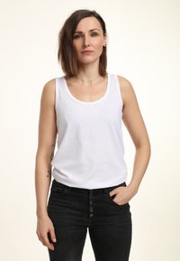 Witte katoenen tanktop met een ronde hals, gecombineerd met hoge zwarte jeans met knoopdetails aan de voorkant.