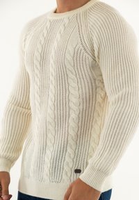 Maglione lavorato a maglia crema con texture a treccia e righe, scollatura rotonda e maniche aderenti. Presenta un piccolo etichetta del marchio sul davanti.