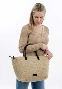 Beige textured tote bag with black leather straps. Features a soft, fluffy surface and a rectangular shape, suitable for daily use.