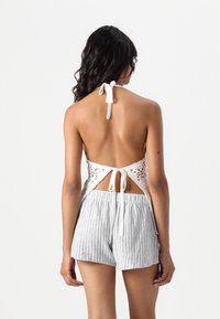 Hvit heklet halterneck topp med åpen rygg og knytting, kombinert med lysegrå stripete shorts. Myk tekstur og uformell design.